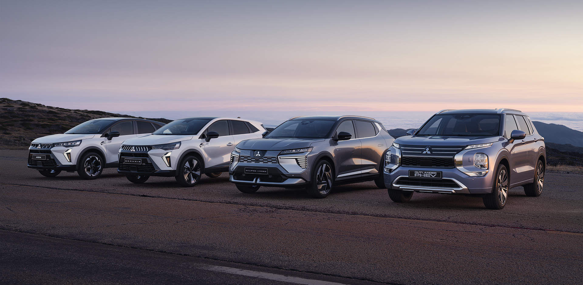 Die Mitsubishi Modell-Range Die Mitsubishi ASX, Grandis, Eclipse Cross und Outlander stehen in der Dämmerung am Straßenrand.