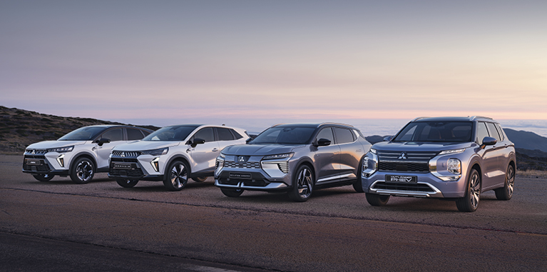 Startseite: Range Vier Mitsubishi Modelle, darunter der Grandis, ASX, Eclipse Cross und Outlander, stehen nebeneinander auf einem offenen Platz vor weiter Landschaft bei Sonnenuntergang.
