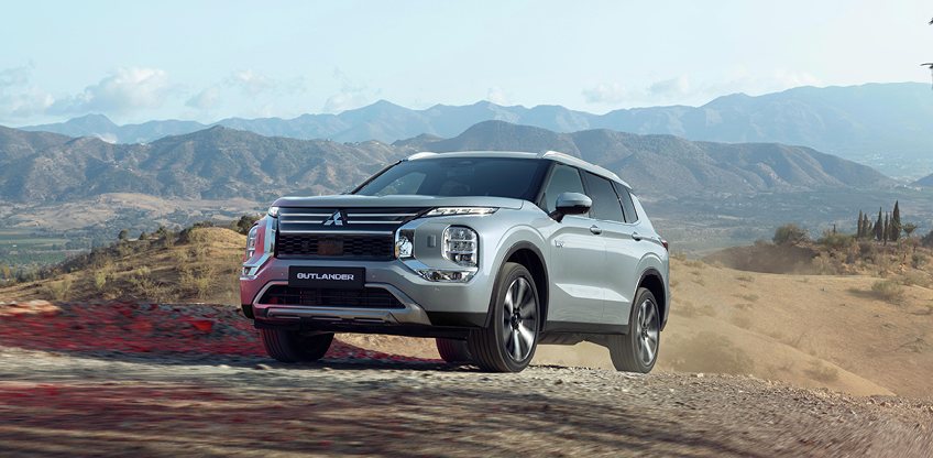 Mitsubishi Outlander Select Frontansicht in der Natur Silberner Mitsubishi Outlander Select in der Frontansicht auf unbefestigtem Gelände mit Bergpanorama im Hintergrund