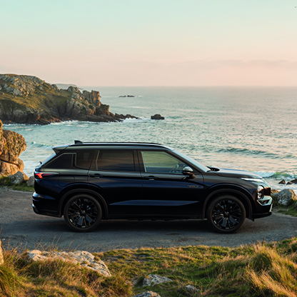 Mitsubishi Outlander Black an der Küste Schwarzer Mitsubishi Outlander Black in der Seitenansicht auf einem felsigen Küstenweg mit Meerblick im Hintergrund
