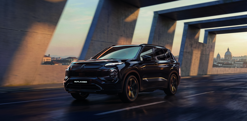 Mitsubishi Outlander Black in der Stadt Schwarzer Mitsubishi Outlander Black in dynamischer Frontansicht unter einem modernen Brückenbauwerk im urbanen Stadtumfeld bei Abenddämmerung