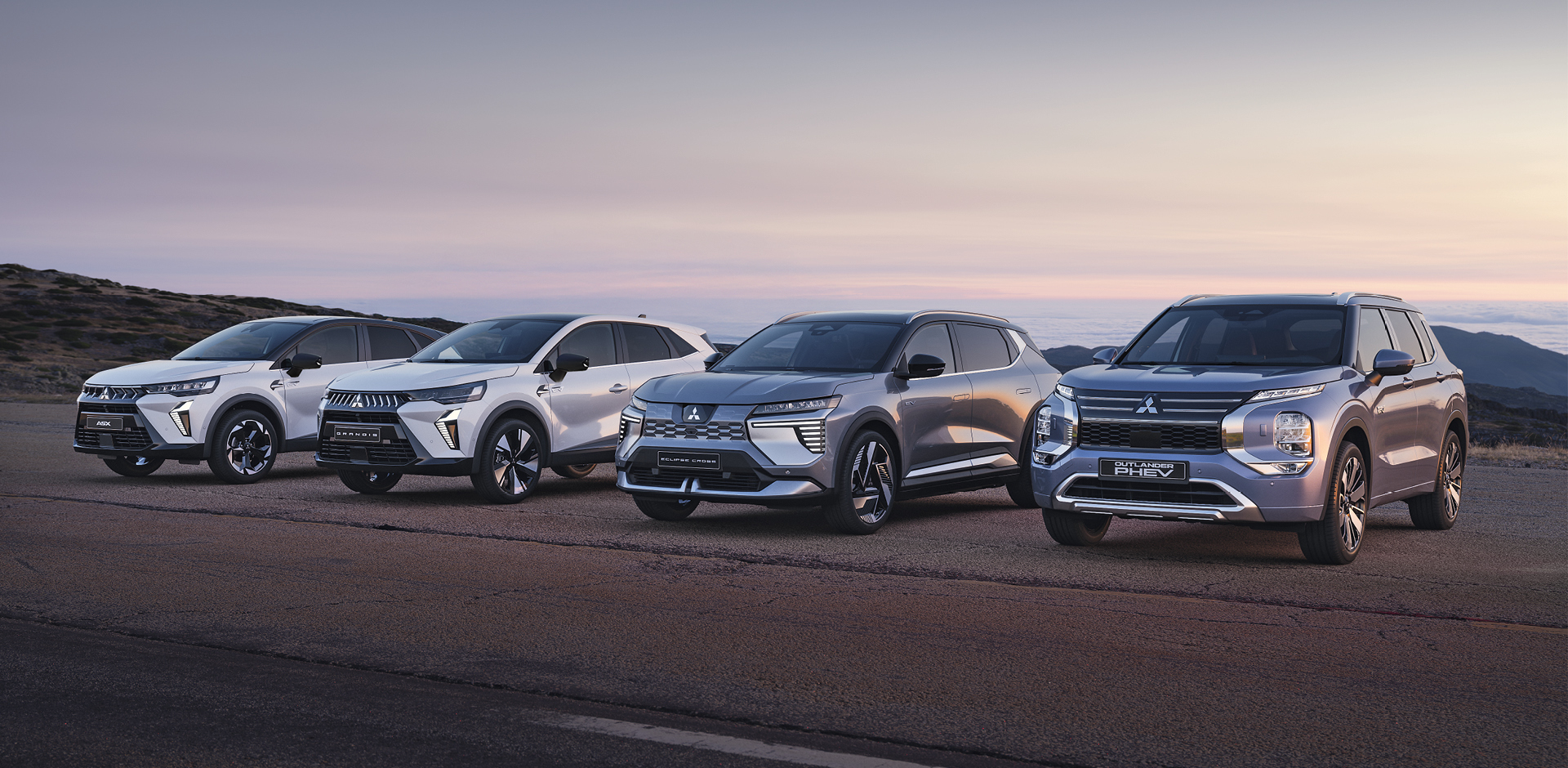 Geschäftskunden: Header Vier Mitsubishi Modelle, darunter der Grandis, ASX, Eclipse Cross und Outlander, stehen nebeneinander auf einem offenen Platz vor weiter Landschaft bei Sonnenuntergang.