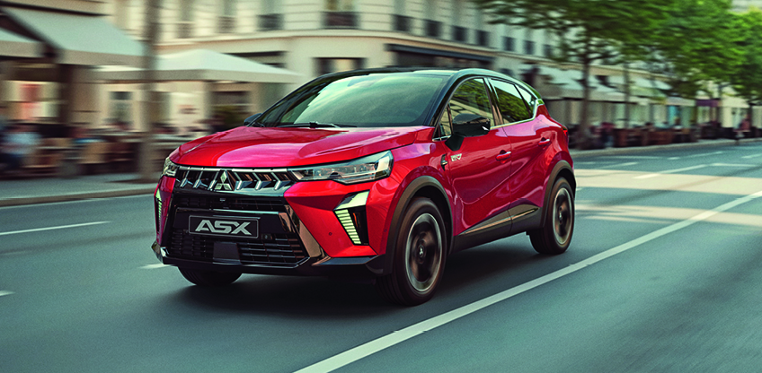 Der Mitsubishi ASX Select – dynamischer Auftritt auf der Stadtboulevard Roter Mitsubishi ASX Select in schräger Front Seitenansicht fährt dynamisch über einen breiten Stadtboulevard, im Hintergrund Straßencafés, Fußgänger und Bäume – betont das moderne, urbane Design des kompakten SUV.