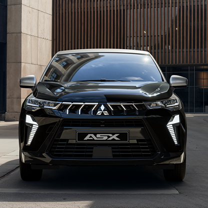 Mitsubishi ASX Black – urbane Frontansicht Frontansicht eines Mitsubishi ASX Black, der in einer modernen Stadtpassage mit hohen Gebäuden und Holzfassade steht; das Bild hebt den markanten Kühlergrill, die LED Signatur und den hochwertigen Auftritt des Sondermodells hervor.