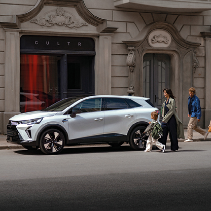 Mitsubishi Grandis Intro Edition im Stadtleben Weißer Mitsubishi SUV in der Seitenansicht, geparkt in einer Stadtstraße vor einem Gebäude, mit einer Frau und einem Kind sowie einem weiteren Passanten im Hintergrund