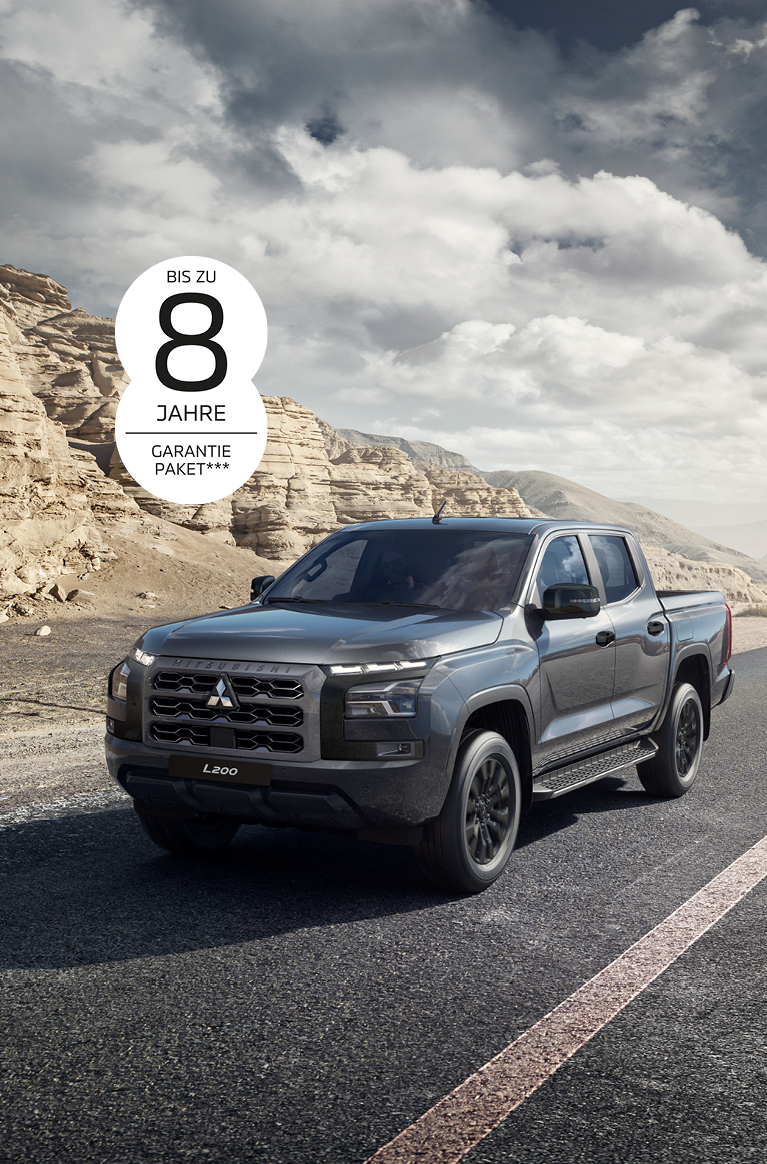 Der kraftvolle L200 Grauer Mitsubishi L200 Pick-up in Front-Seitenansicht auf einer asphaltierten Straße durch eine karge Felslandschaft; oben links ist der Hinweis „Bis zu 8 Jahre Garantiepaket***“ zu sehen.