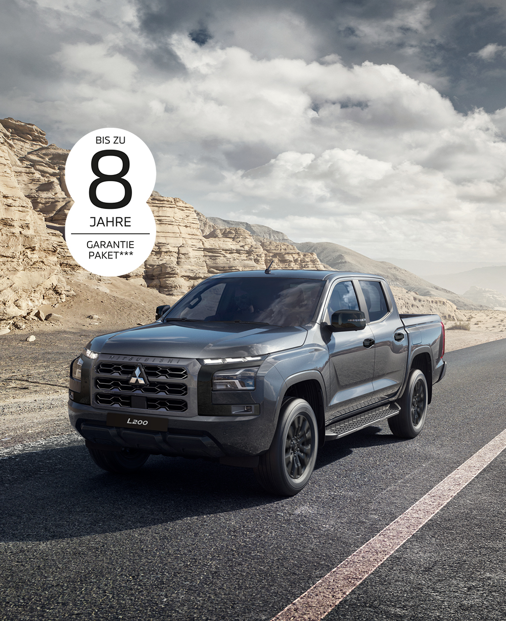 Der kraftvolle L200 Grauer Mitsubishi L200 Pick-up in Front-Seitenansicht auf einer asphaltierten Straße durch eine karge Felslandschaft; oben links ist der Hinweis „Bis zu 8 Jahre Garantiepaket***“ zu sehen.
